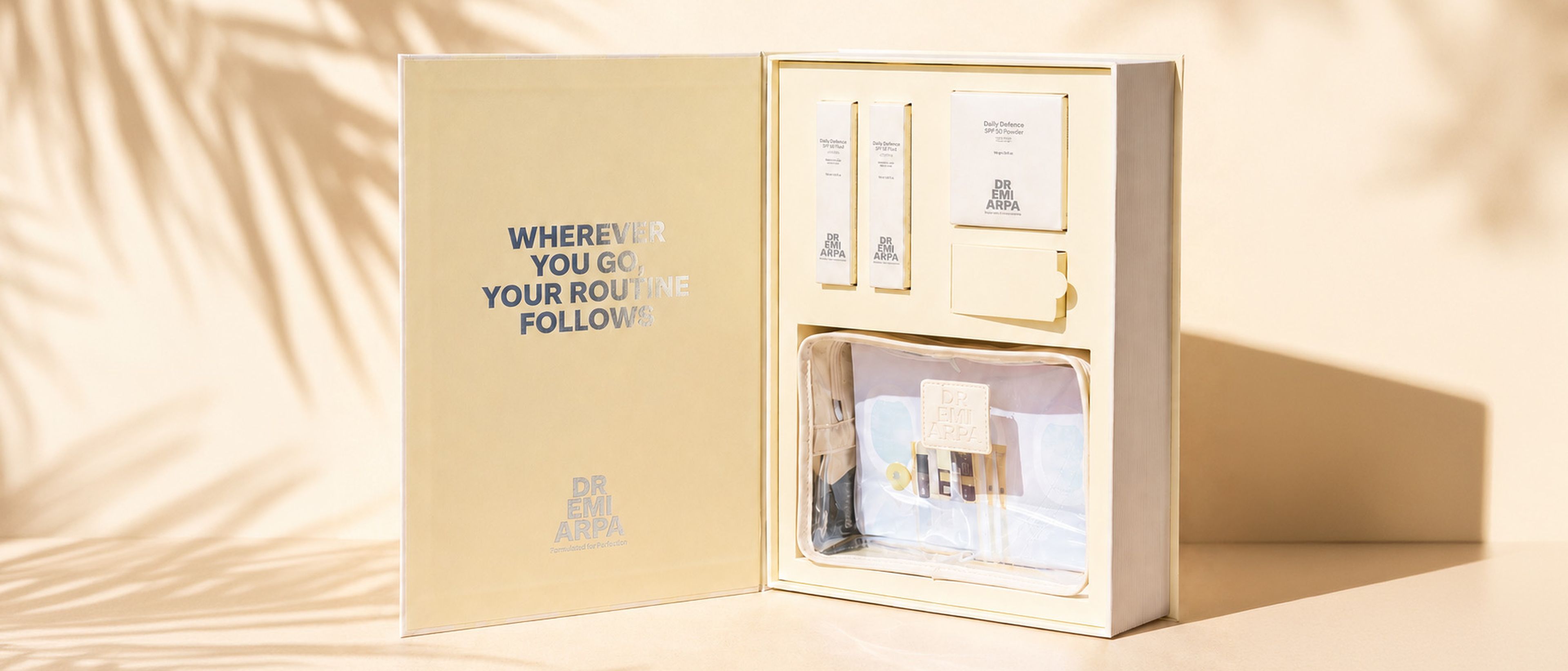 Offene Hautpflege-Set-Box mit verschiedenen Produkten darin, beschriftet mit „WHEREVER YOU GO, YOUR ROUTINE FOLLOWS“. Deutlicher Schatten von Palmblättern.