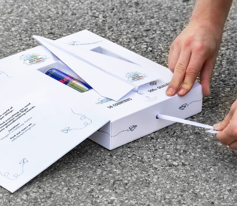 Geöffnete Einladungs-Box für Red Bull Paper Wings Finale 2022 mit flugbereitem Papierflieger