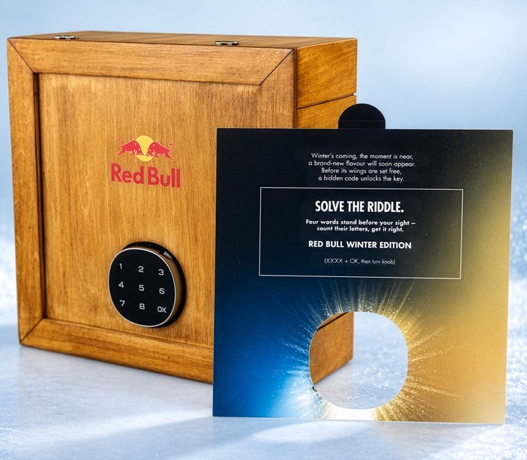 Eine hölzerne Red-Bull-Box mit einem digitalen Schloss, zusammen mit einer Rätselkarte, die für die Red-Bull-Winteredition wirbt.