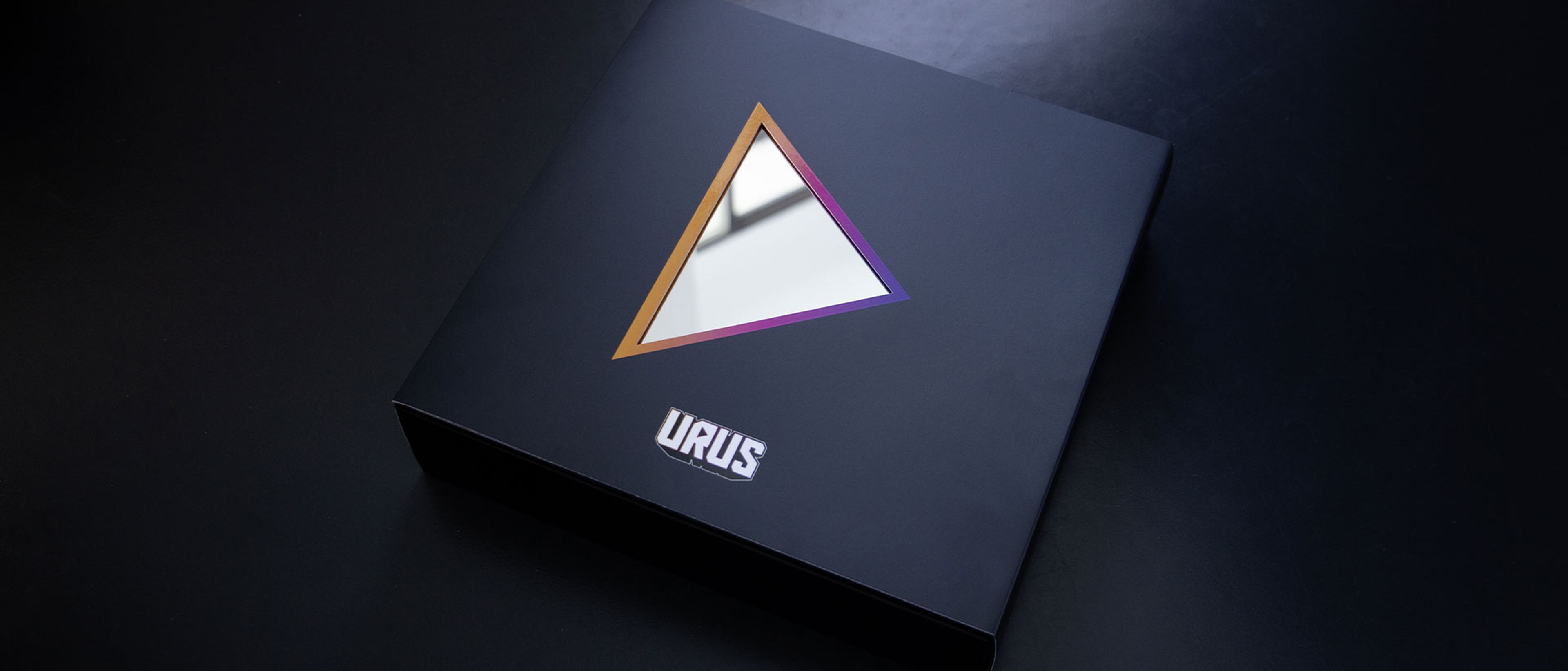 Schwarze Box mit farbig umrandetem dreieckigem Spiegel und Aufschrift "URUS"