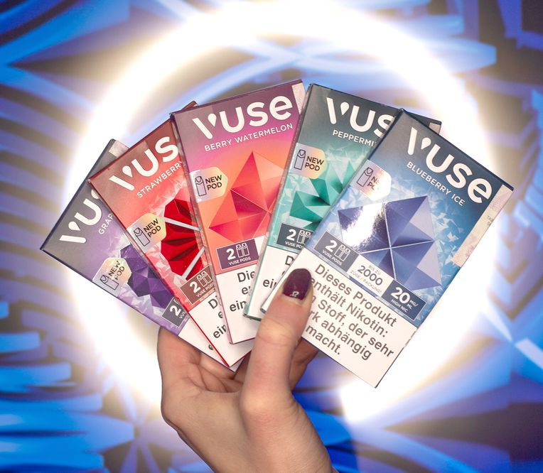 Eine Hand hält vier Vuse-Vape-Pod-Packungen in verschiedenen Geschmacksrichtungen vor einem blauen, abstrakten Hintergrund.