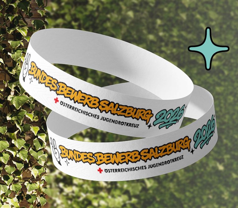 Zwei weiße Armbänder mit den Aufschriften „Bundesbewerb Salzburg 2026“ und „Österreichisches Jugendrotkreuz“ vor dem Hintergrund von mit Efeu bewachsenen Ziegelsteinen.