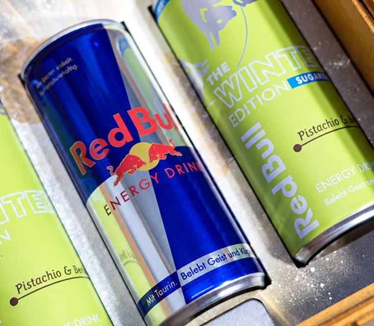 Drei Red-Bull-Dosen, davon zwei grüne „Winter Edition“ mit Pistaziengeschmack und eine im klassischen blau-silbernen Design.