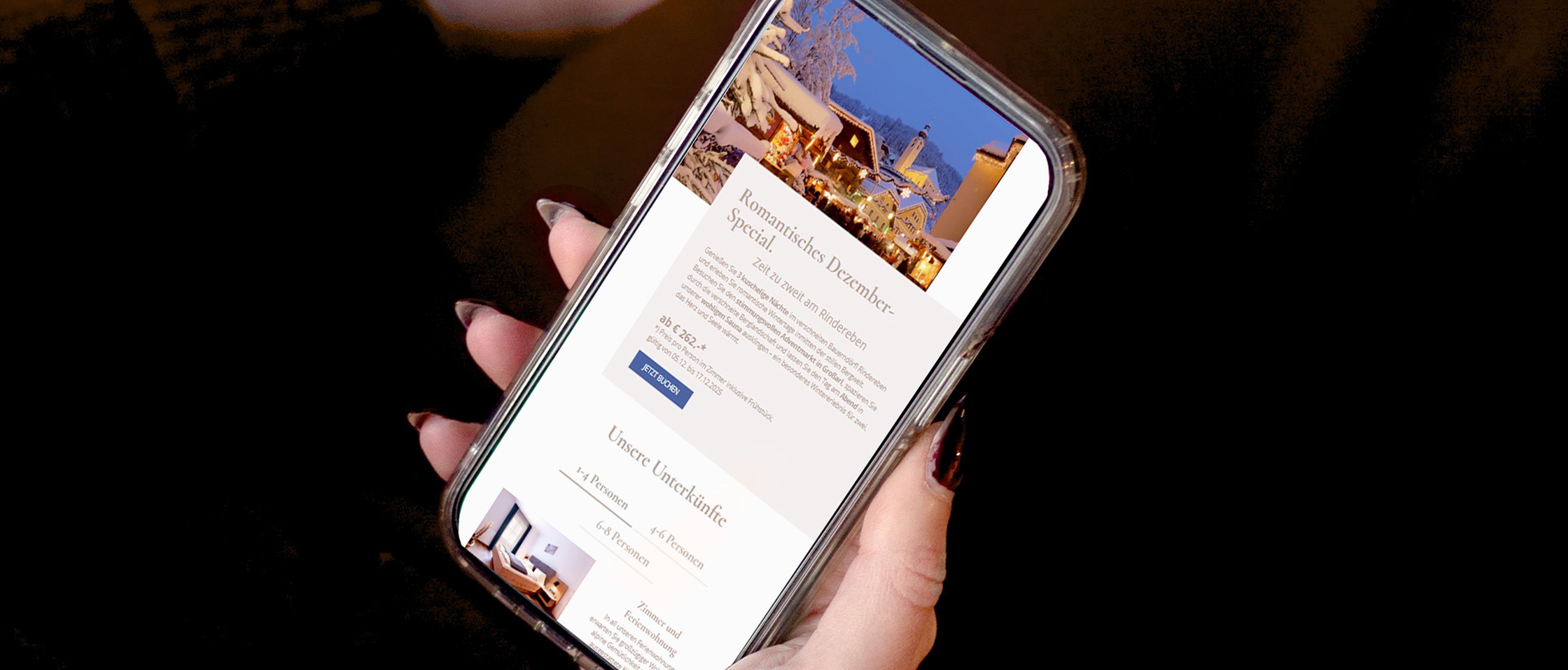 Eine Person, die ein Smartphone in der Hand hält, auf dessen Bildschirm ein Weihnachtsangebot mit dem Bild eines verschneiten Dorfes zu sehen ist.