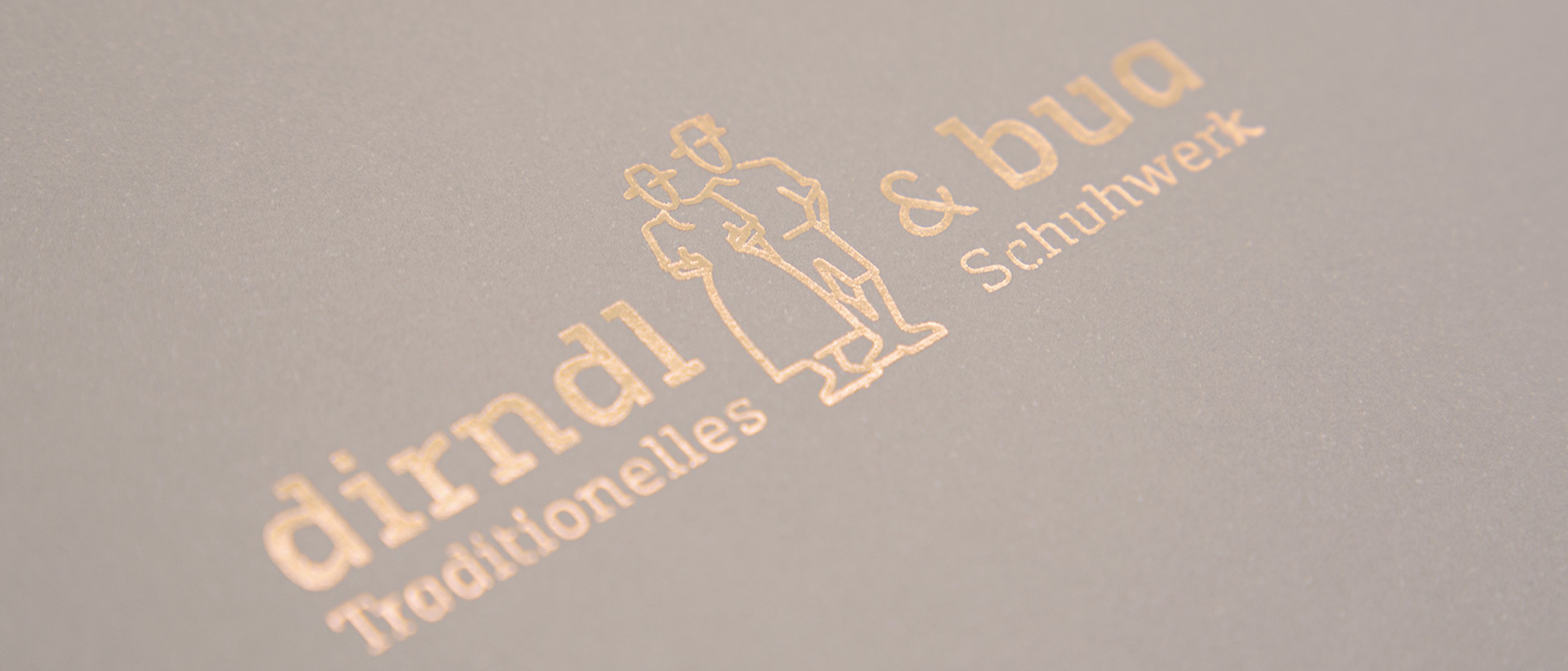 Goldenes Logo von dirndl & bua auf beigem Papier