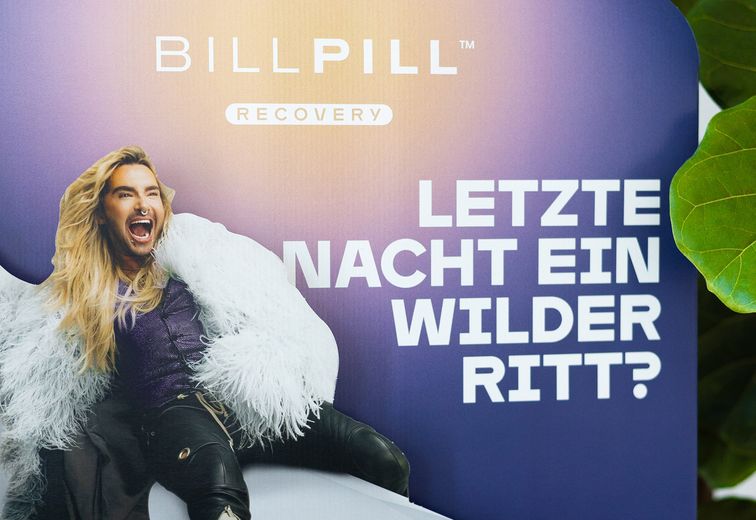 Eine Person mit langen blonden Haaren und einem Nasenring posiert begeistert vor einem violetten Hintergrund, auf dem deutscher Text und die Worte „BillPill Recovery“ zu sehen sind.